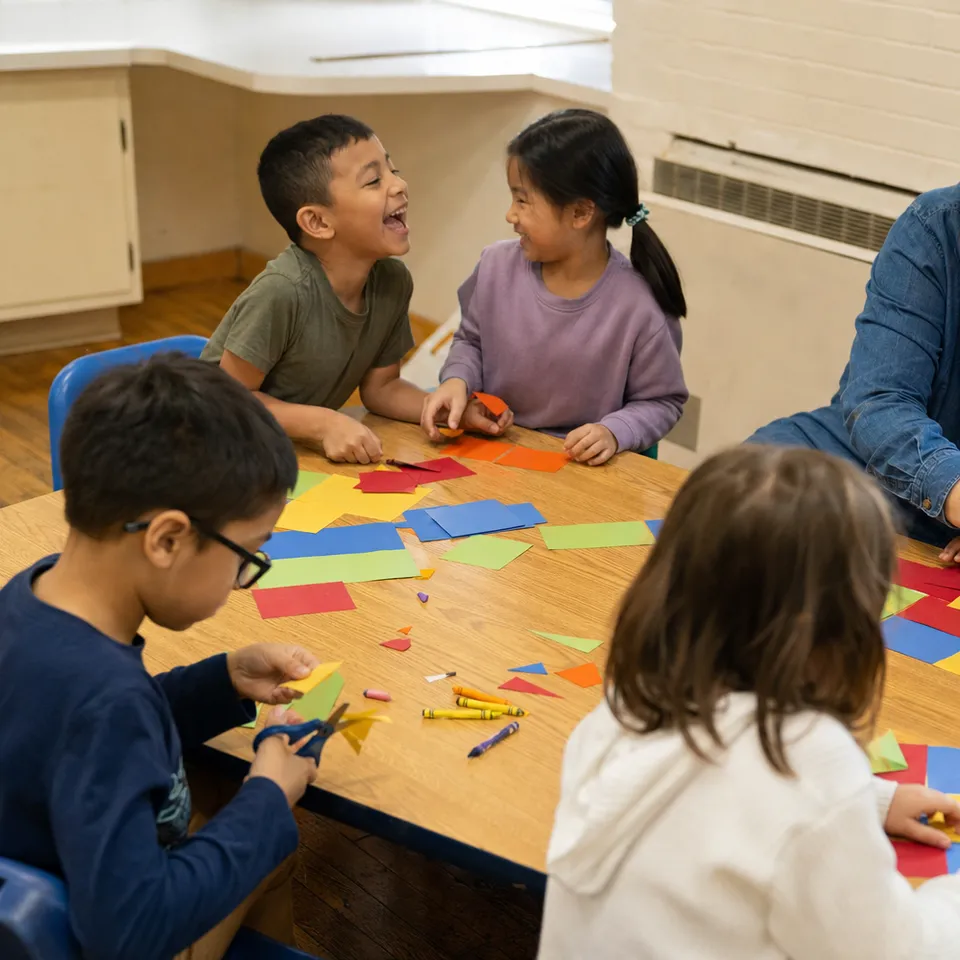 Three children at a table covered in colored paper squares, two of them laughing.